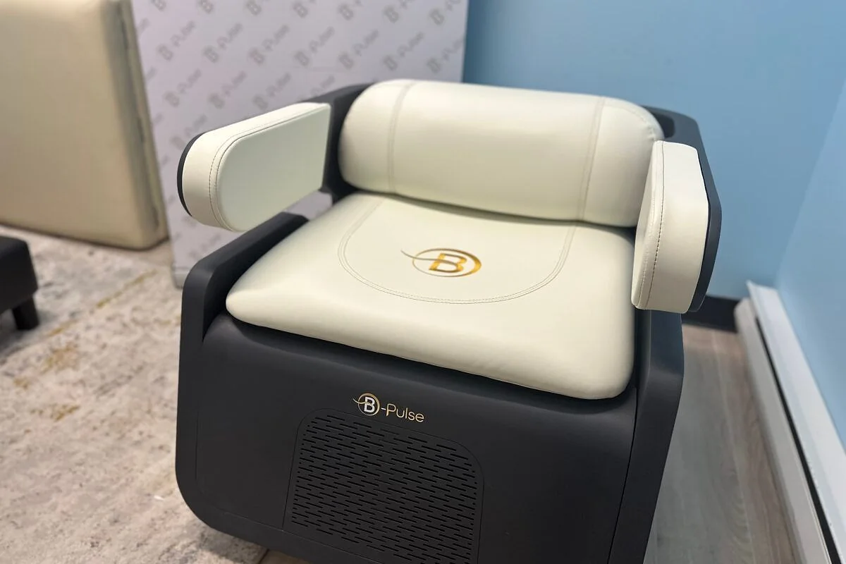 La chaise B-PULSE en cuir crème, avec l'emblème doré B sur l'assise, installée dans un salon aux murs bleus.
